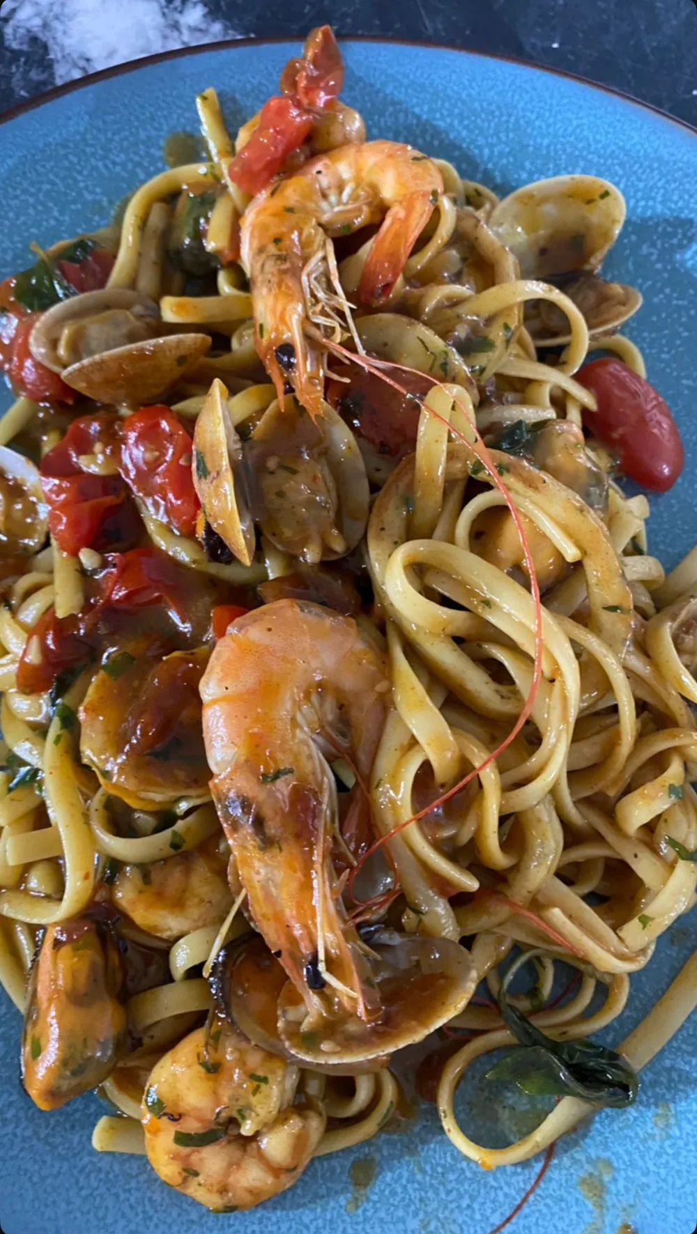 Linguine aux crevettes entières, palourdes, moules et tomates confites dans une assiette bleue