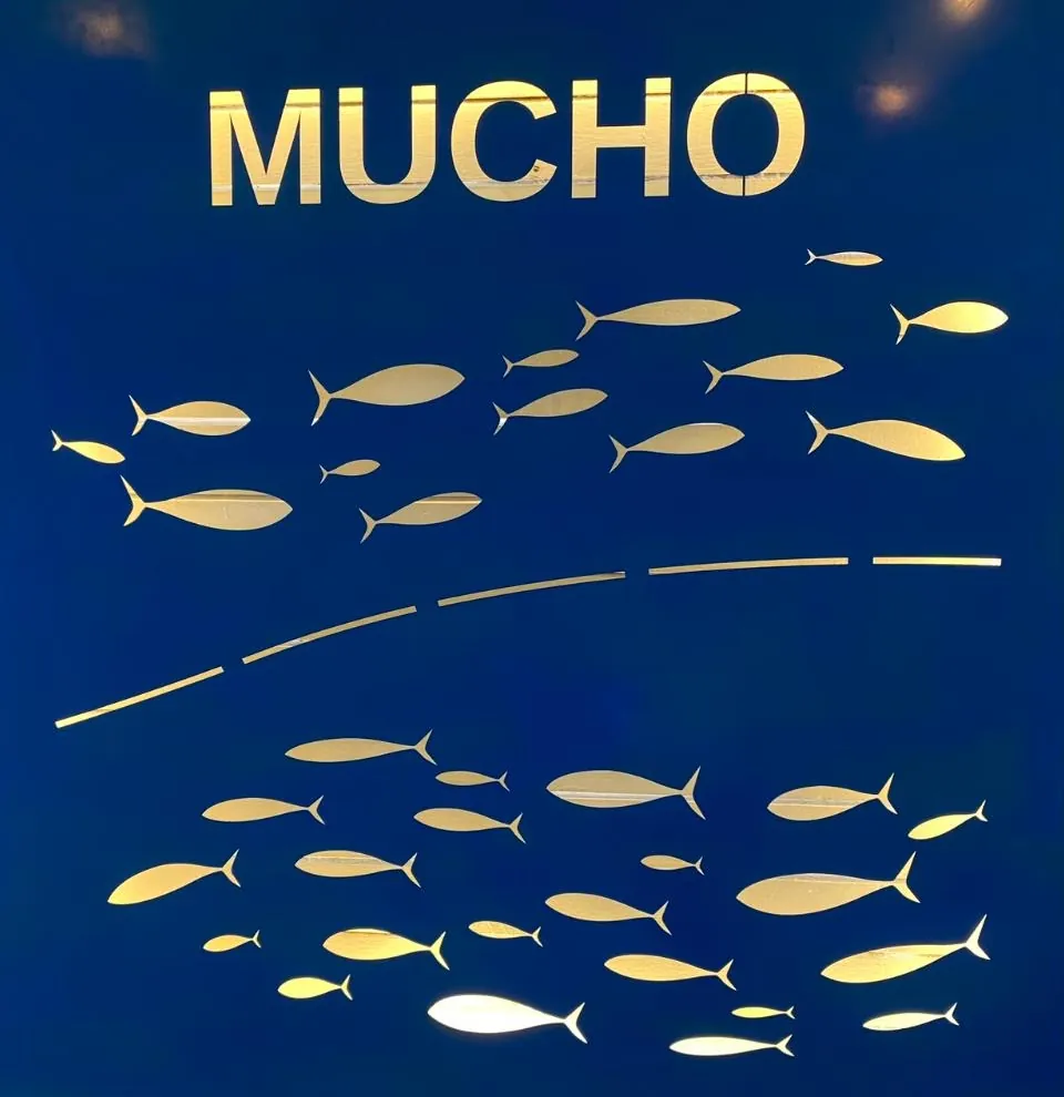 Le décor de Mucho : le nom en lettres dorées au-dessus d'un banc de poissons dorés sur fond bleu marine
